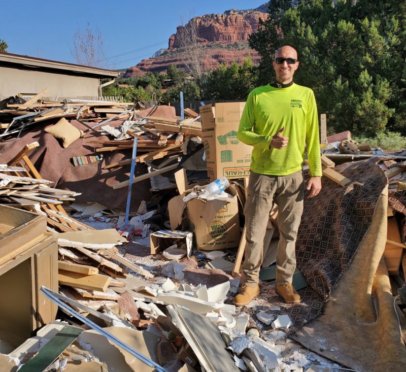 squeaky clean team member standing with construction debris pile that needs to be hauled off